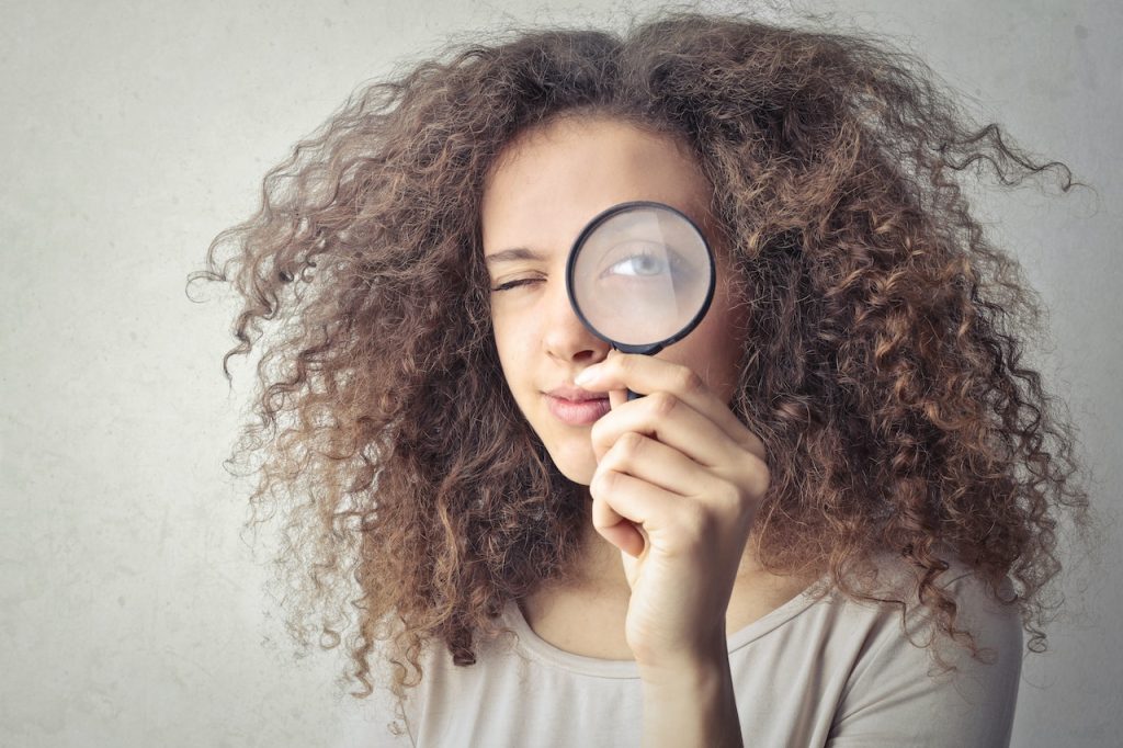 Woman holding magnifying glass to her eye.
