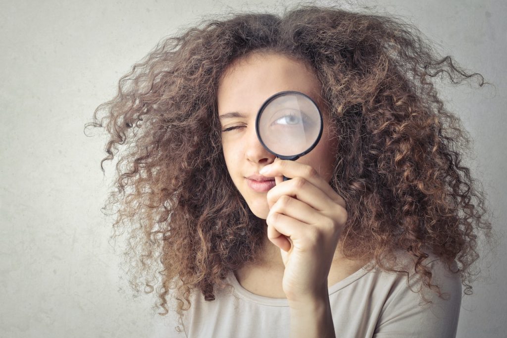 Woman holding magnifying glass to her eye. 